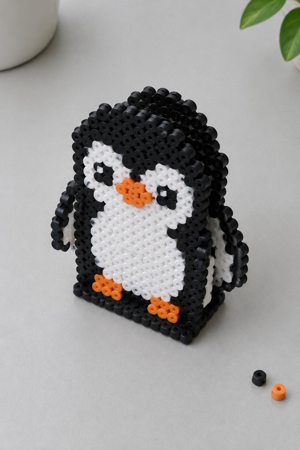 Black and white perler bead penguin with orange beak and feet