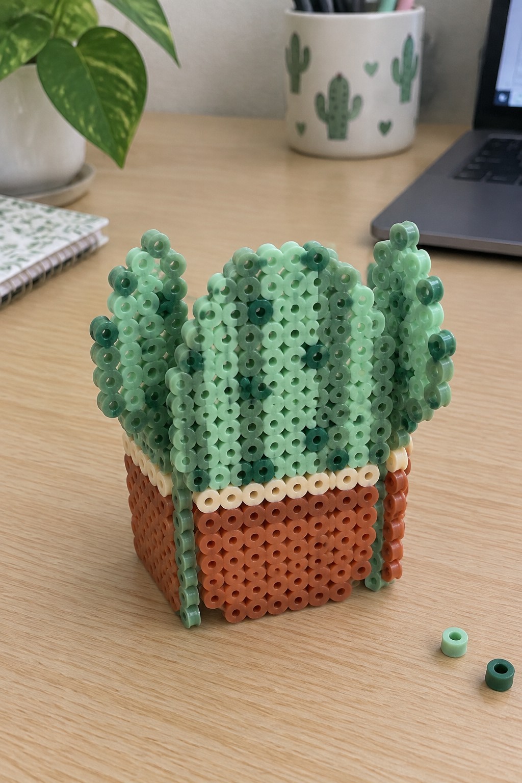 Perler bead cactus in brown pot on wooden desk with loose beads nearby