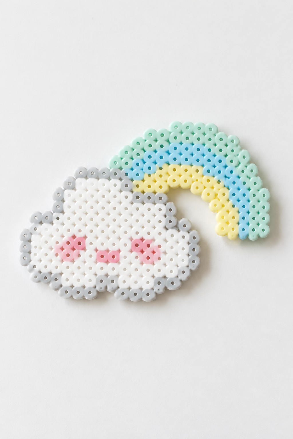 Perler bead cloud with pink cheeks and pastel rainbow arching overhead