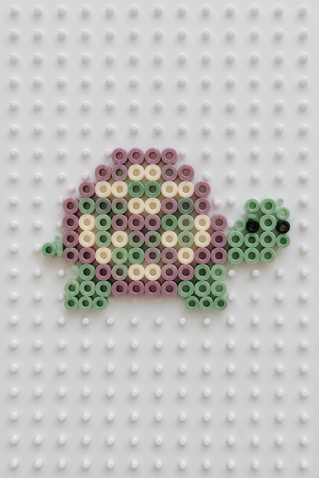 Perler bead turtle in pastel purple, green, and cream on white pegboard.