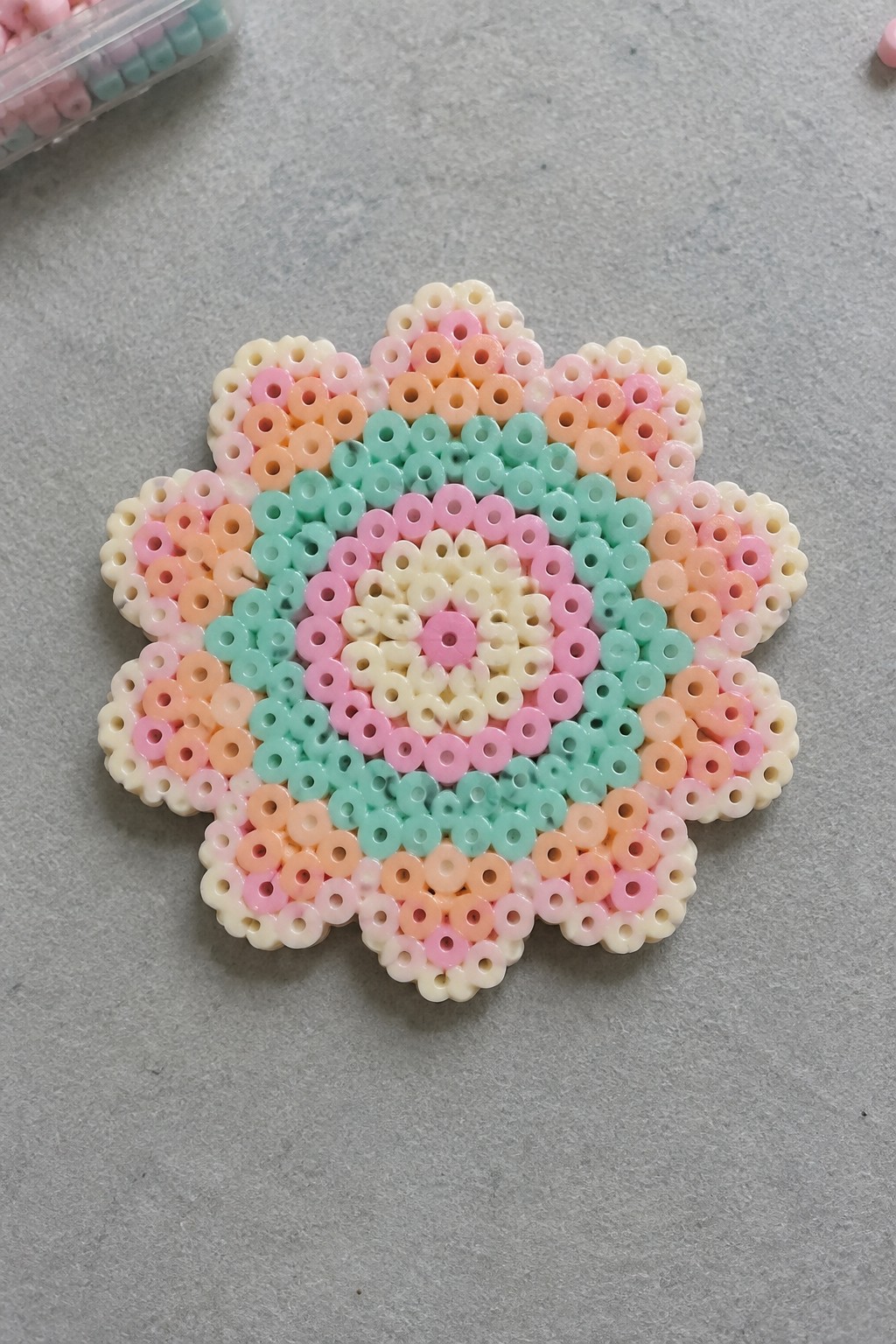 A flower-shaped Perler bead pattern in pastel colors arranged on a pegboard.
