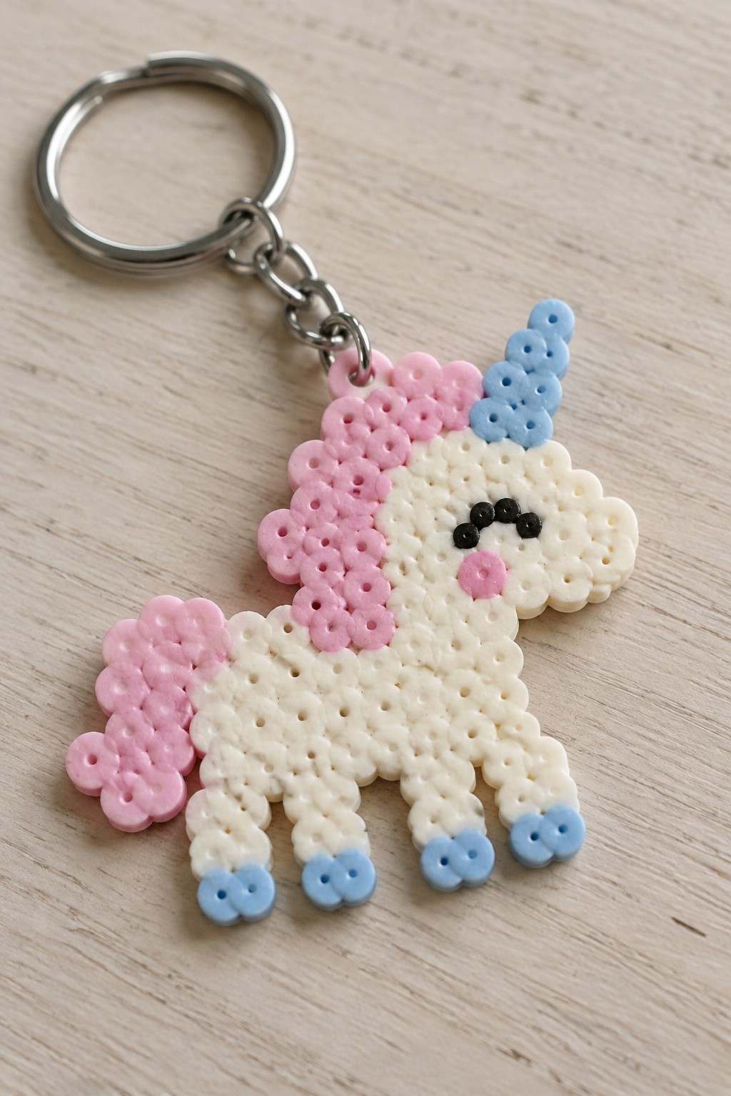Beaded unicorn keychain with pink mane, blue horn, and silver metal ring on wood