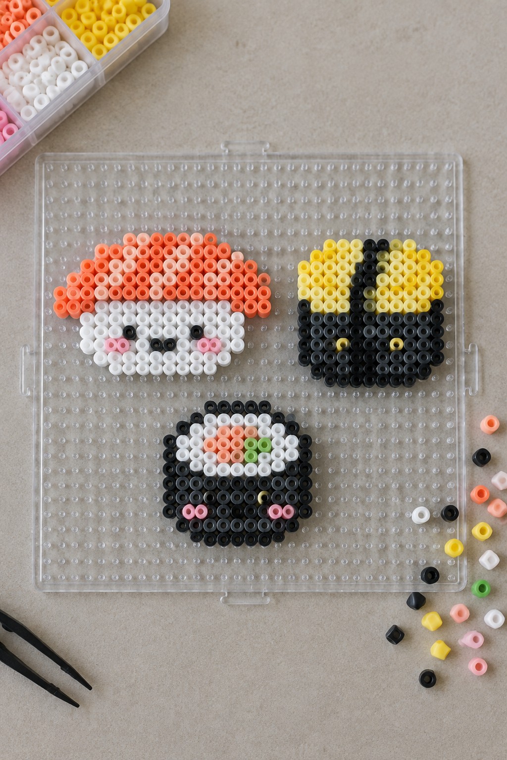 Three unfused Perler bead kawaii designs on a pegboard showing an orange and white animal face, a yellow and black bee, and a sushi roll with a face.