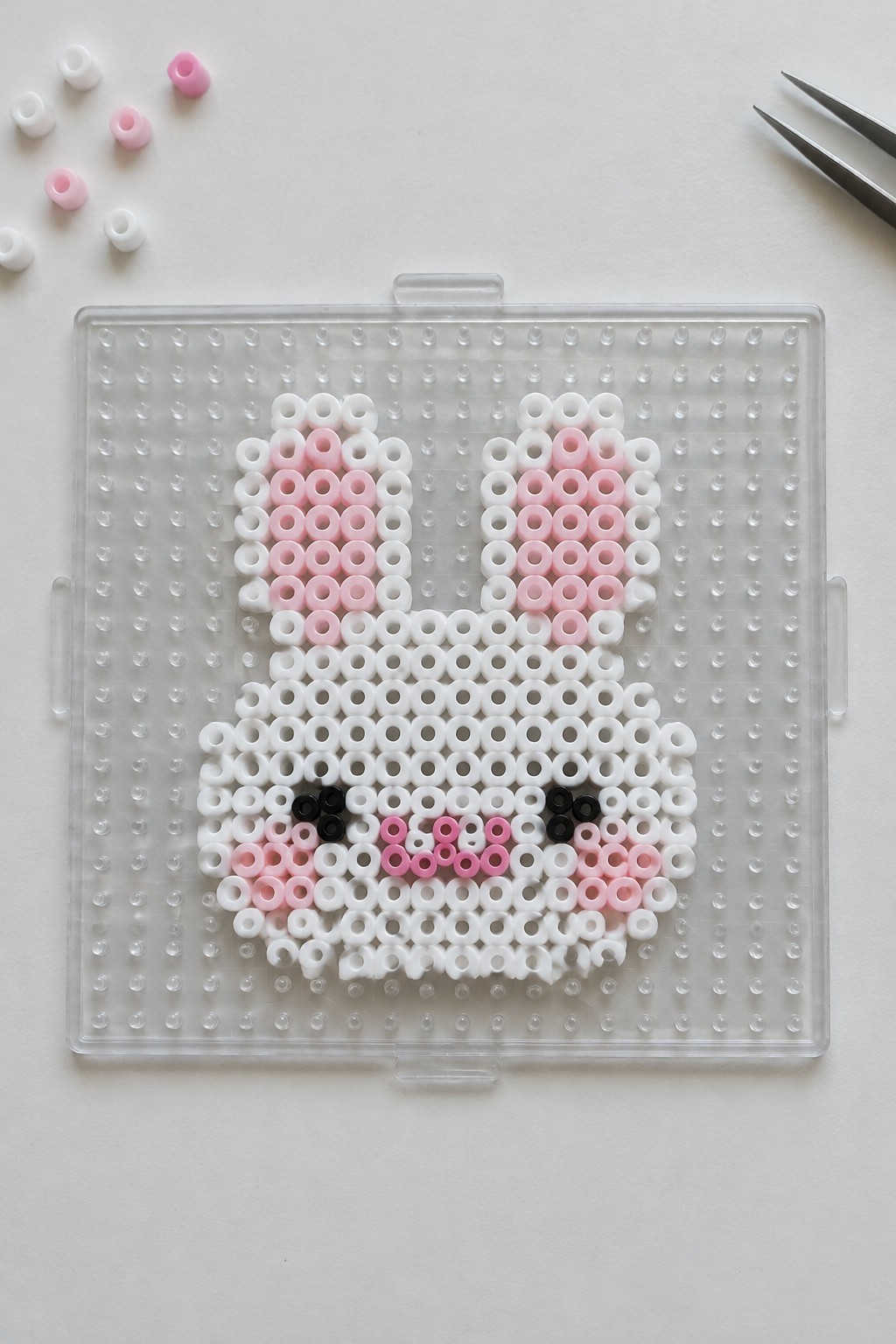 Perler bead kawaii bunny arranged on a clear pegboard using white, pink, and black beads.