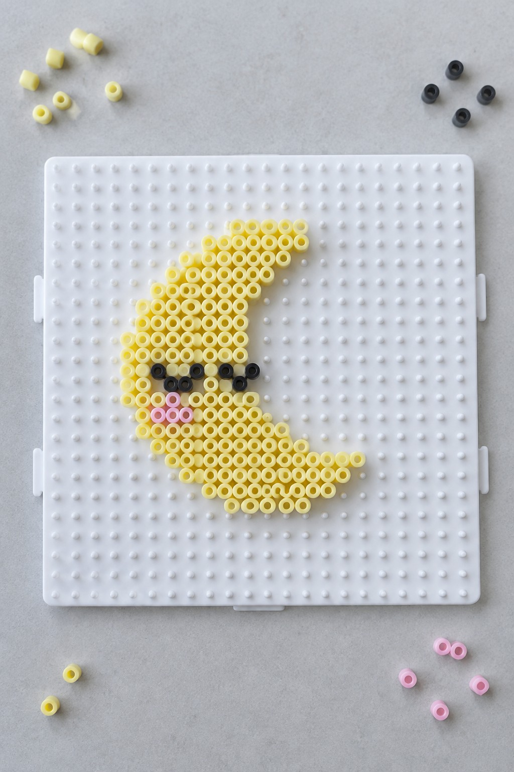 Yellow crescent moon bead art with black eyes and pink cheeks on pegboard