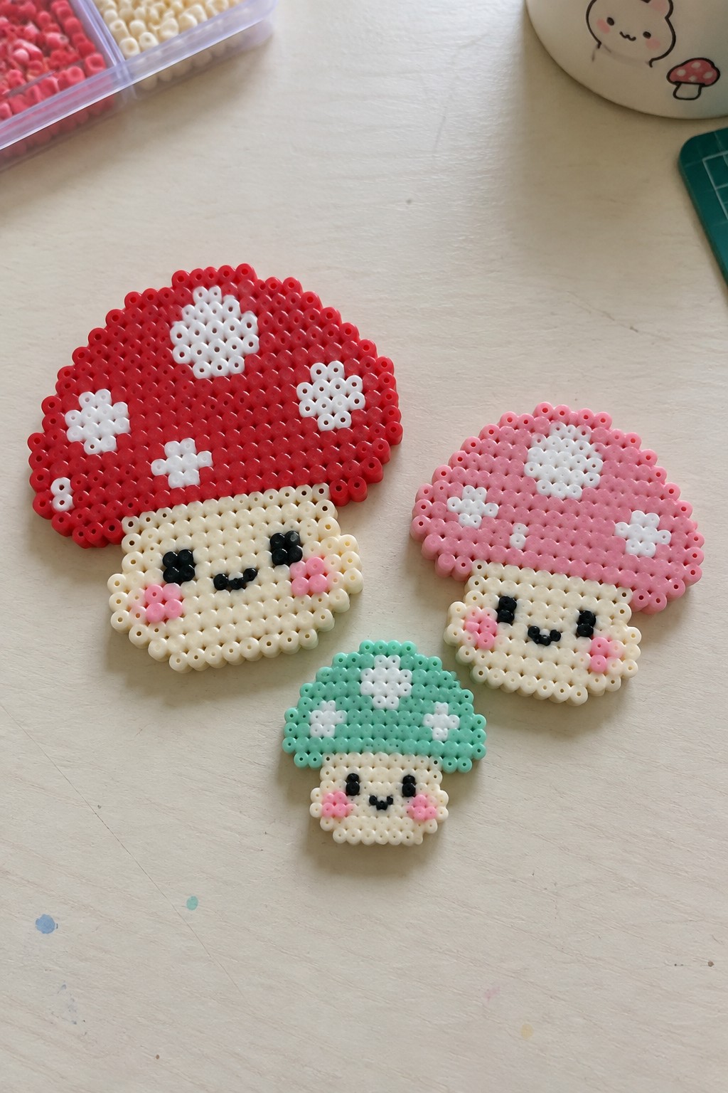 Three perler bead mushrooms with cute faces in red, pink, and green.