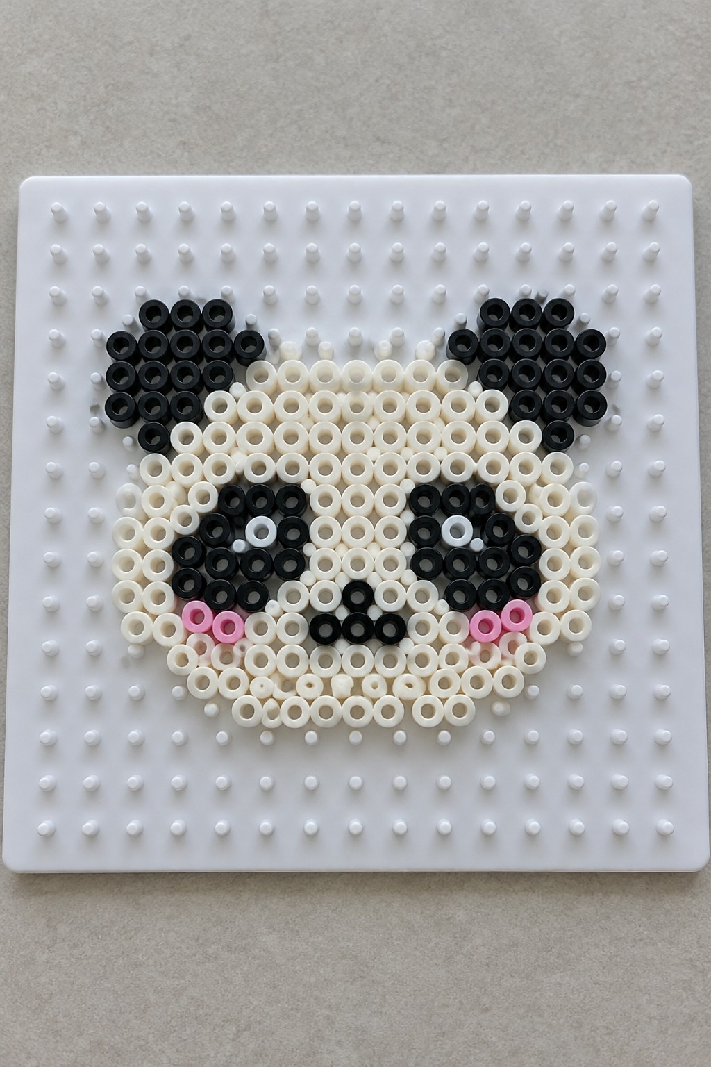 Black and white perler bead animal face with pink cheeks on pegboard