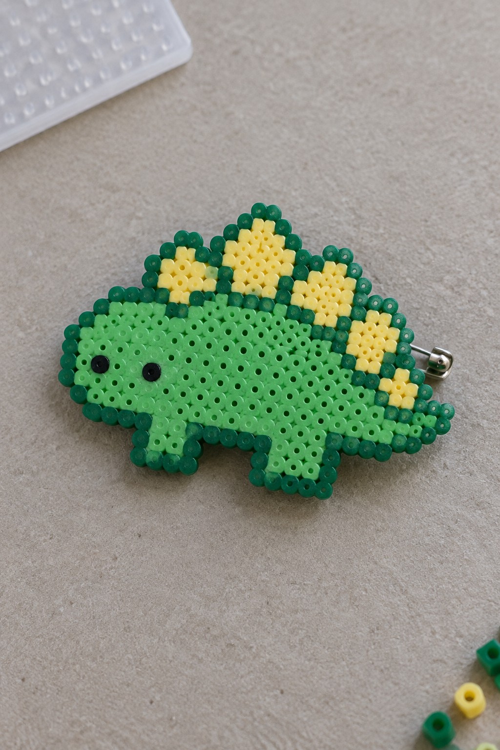Green perler bead dinosaur pin with yellow back plates and black eyes