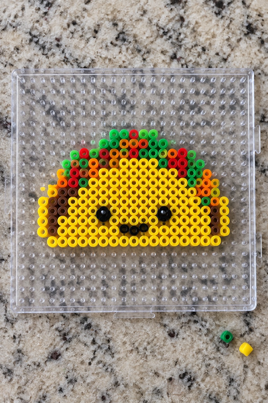 Colorful Perler beads forming a smiling rainbow taco on clear pegboard.