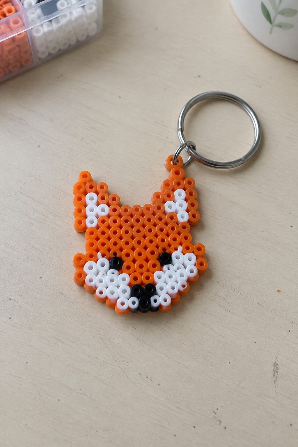 Orange perler bead fox keychain with white black face and silver ring on wood.