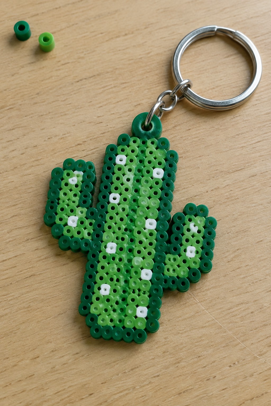 Green Perler bead cactus keychain with metal ring on wooden surface.