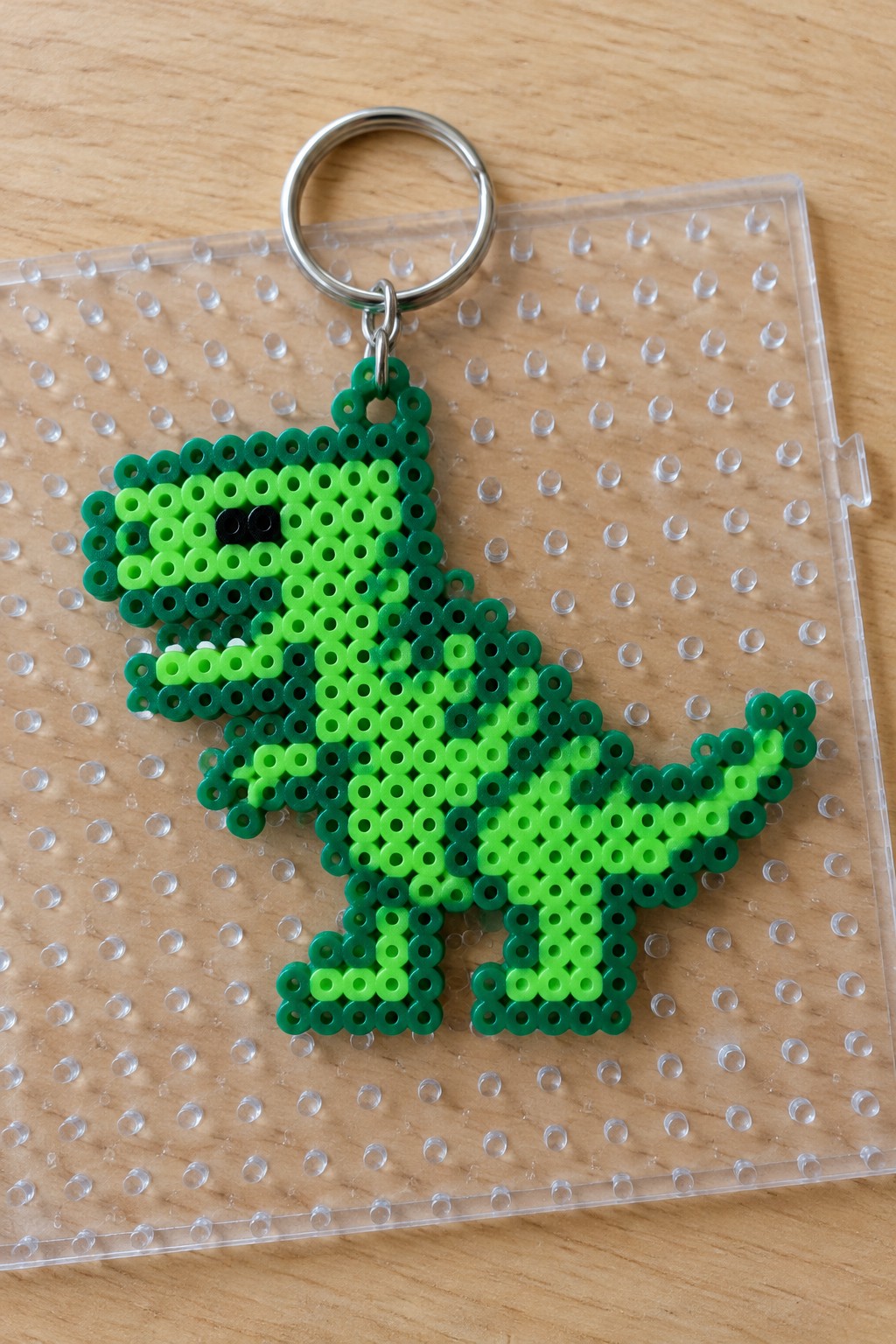 Green perler bead T-rex keychain with metal ring on clear pegboard