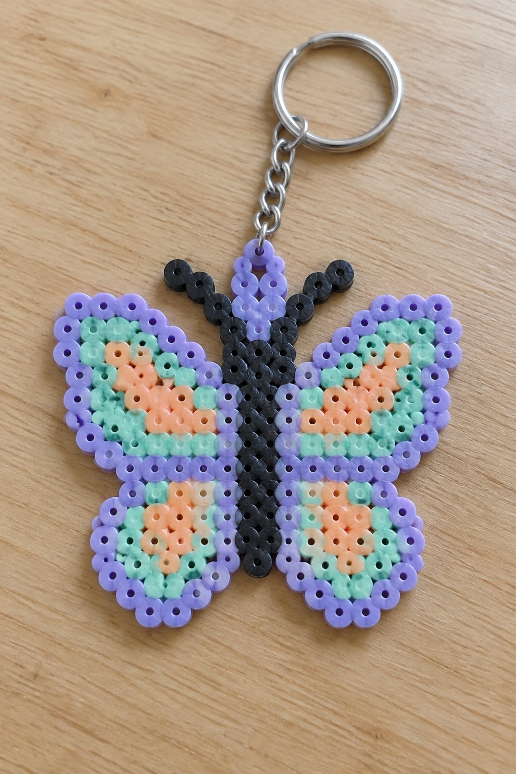 Colorful perler bead butterfly keychain with purple wings and silver ring on wood.