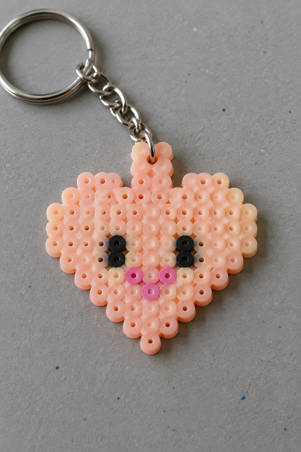 Peach-shaped perler bead keychain with black eyes, pink cheeks, and metal ring