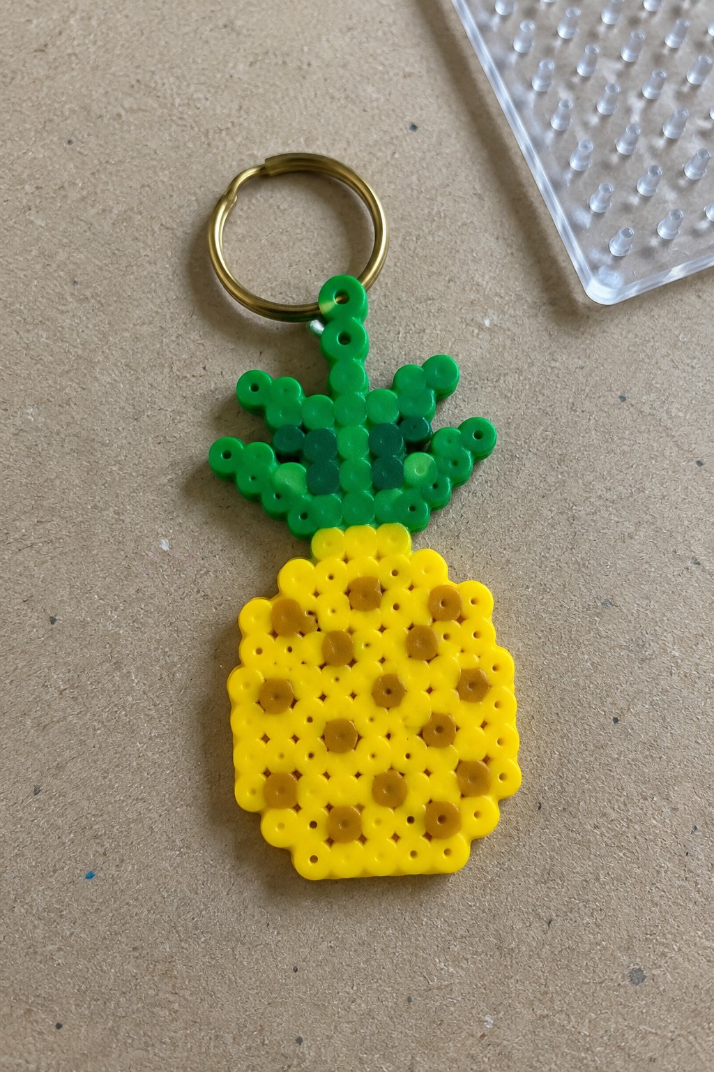 Yellow green perler bead pineapple keychain with gold ring on brown surface
