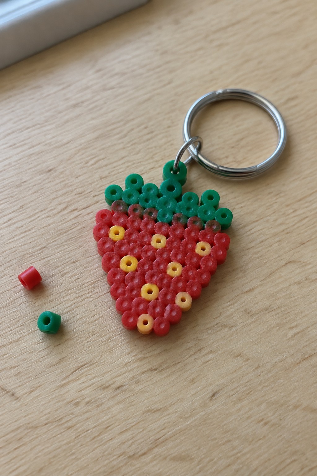 Strawberry Perler bead keychain with red body, yellow seeds, green leaves, metal ring