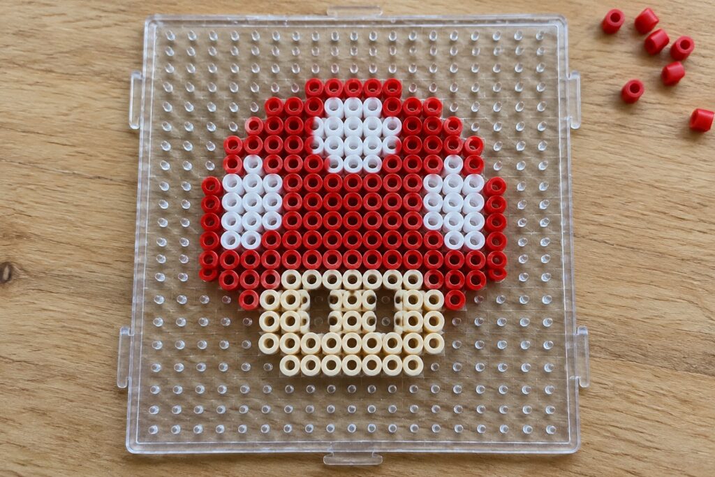 Red and white Poké Ball made of perler beads on clear pegboard