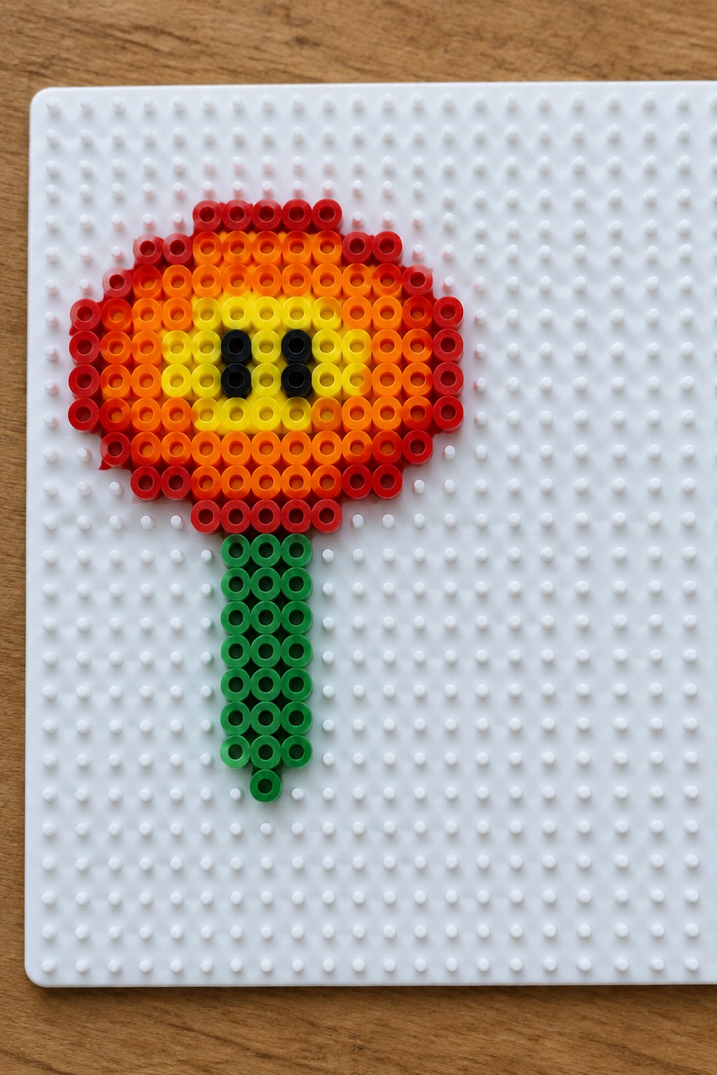 Perler bead flower with red-orange petals, yellow center, black details, and green stem.