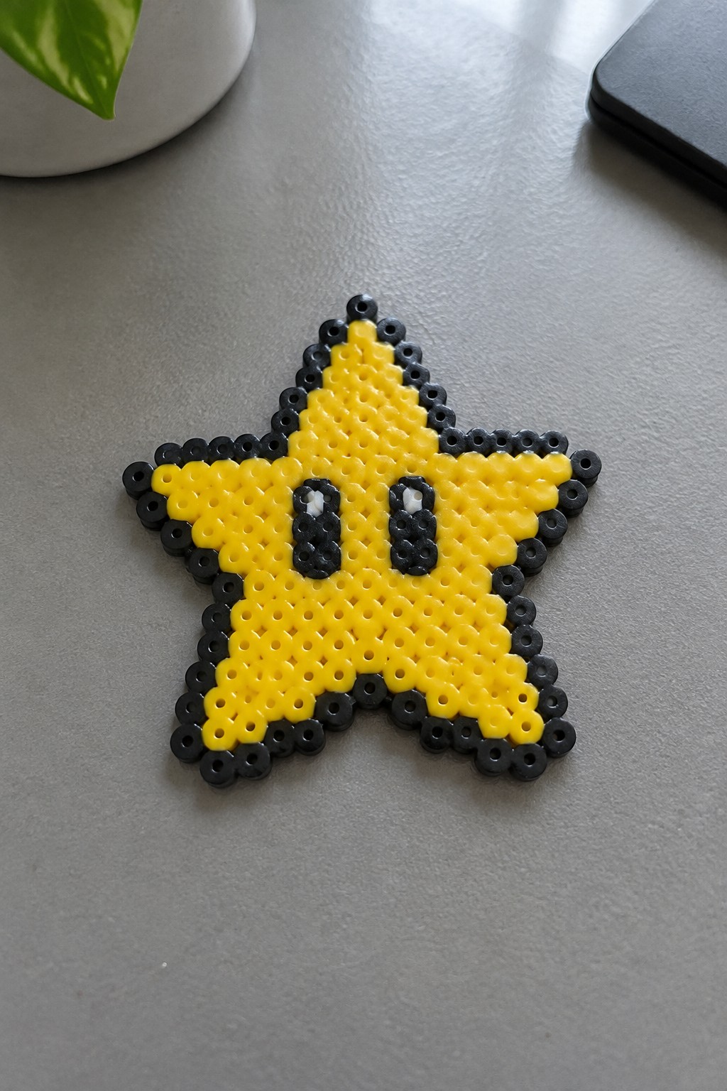 Yellow perler bead star with black outline and cartoon eyes on gray table