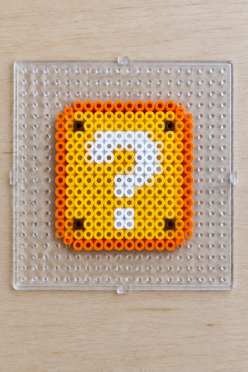 Perler bead fox face in orange, yellow, white, and brown on clear pegboard