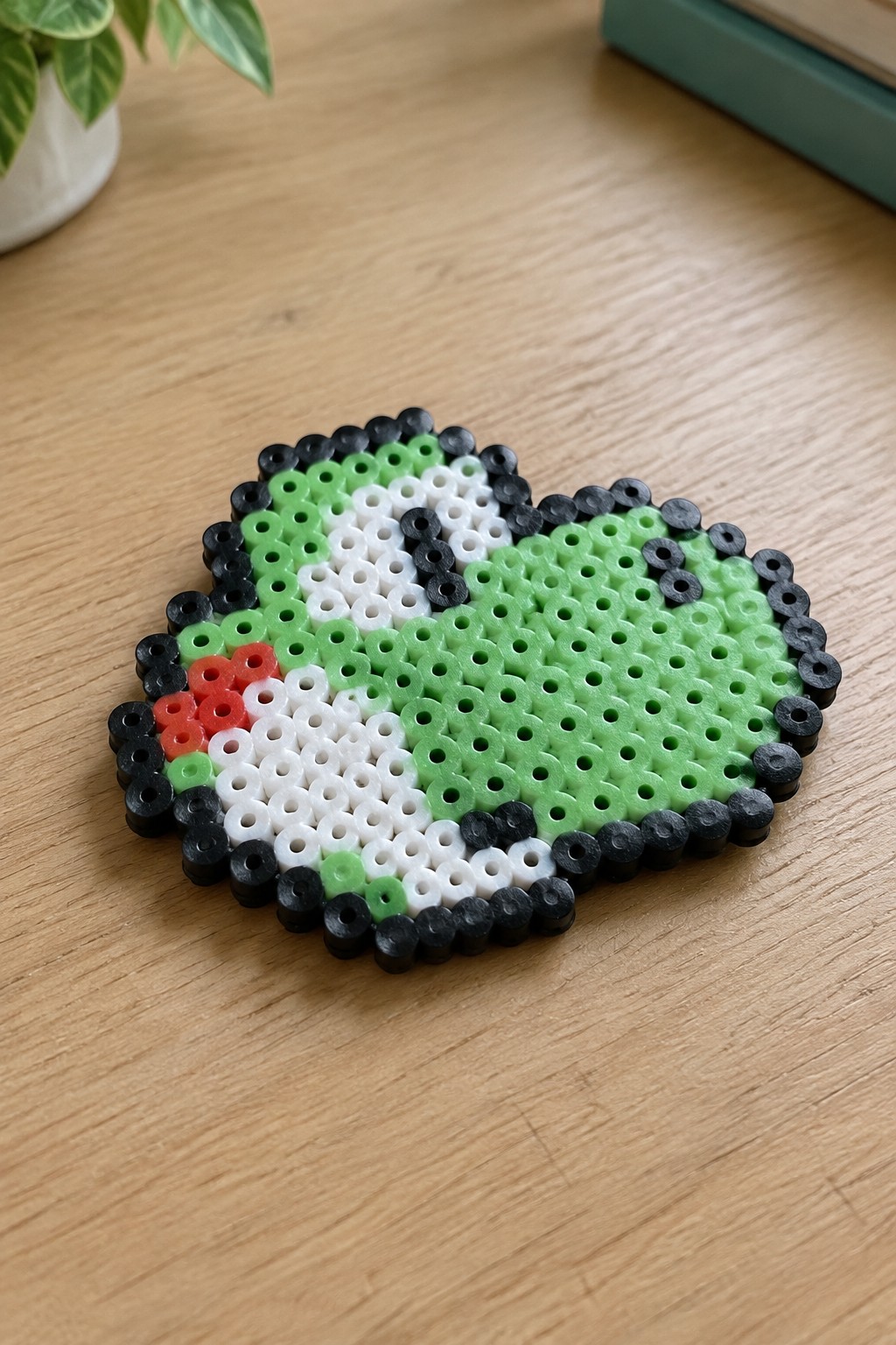 Oval perler bead artwork of green character with black border on wooden table