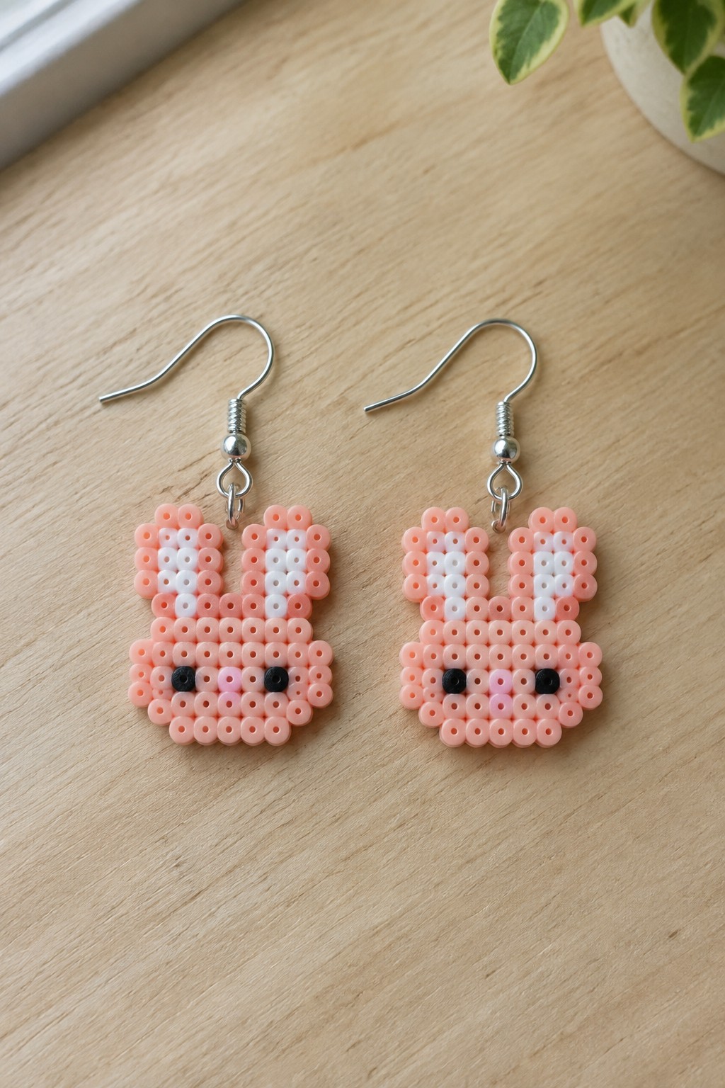 Pair of pink perler bead bunny earrings with white ears and black eyes.