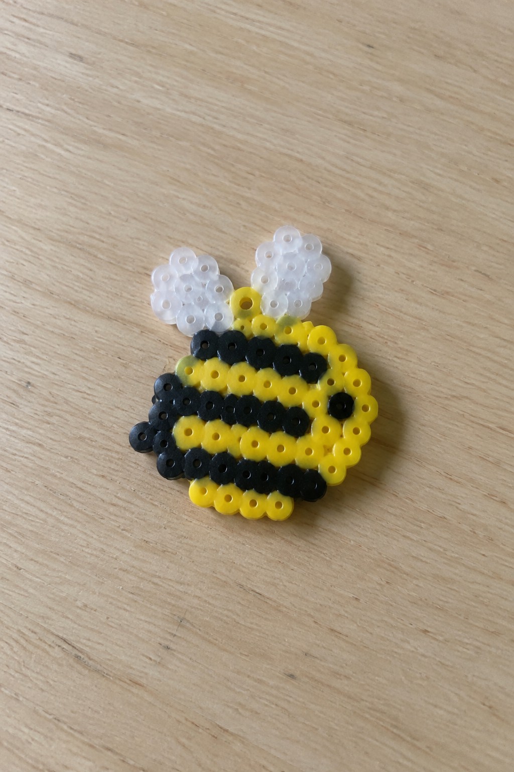 Yellow and black striped perler bead bee with white wings on wood