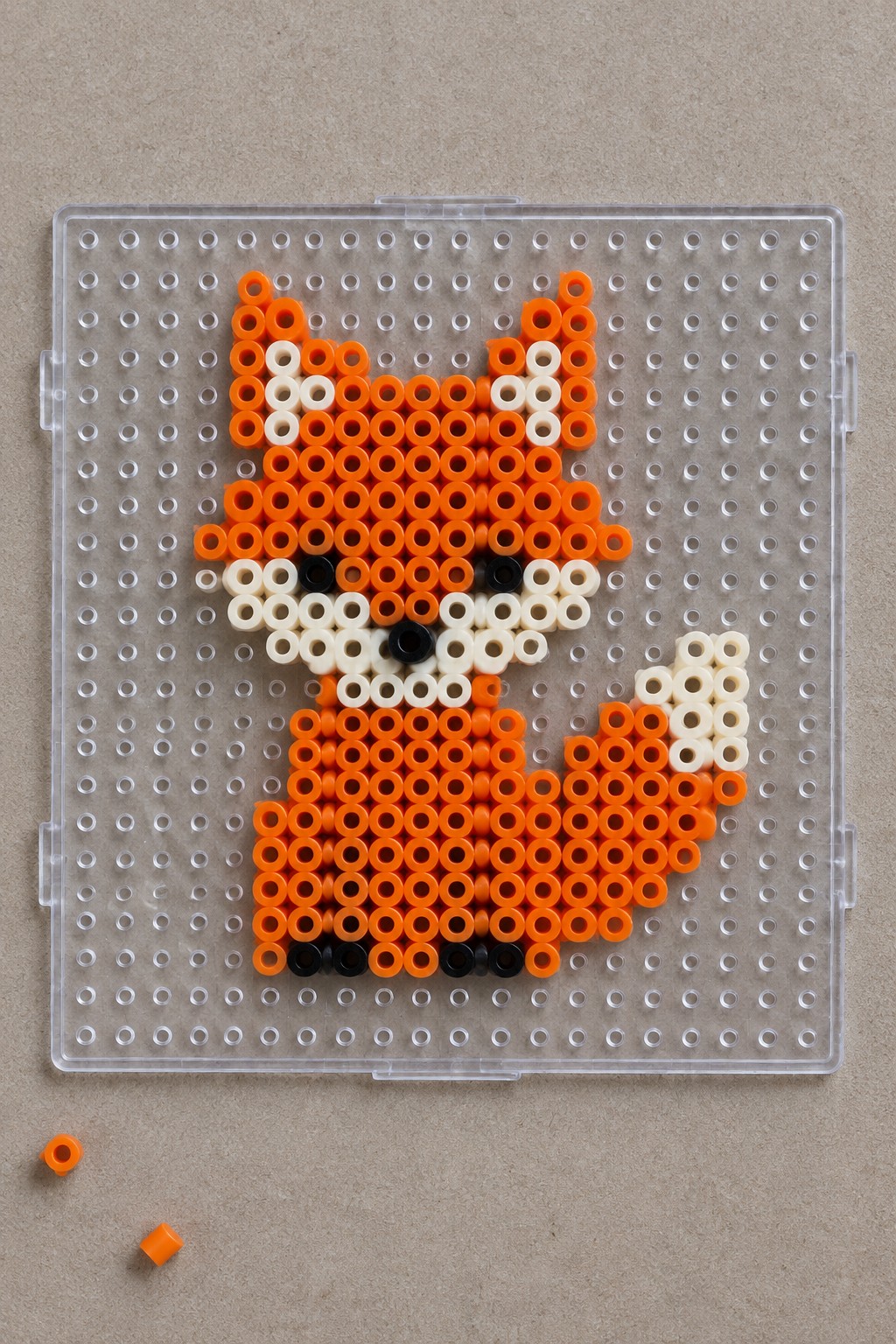 Orange white and black Perler beads arranged as a fox on a clear pegboard.