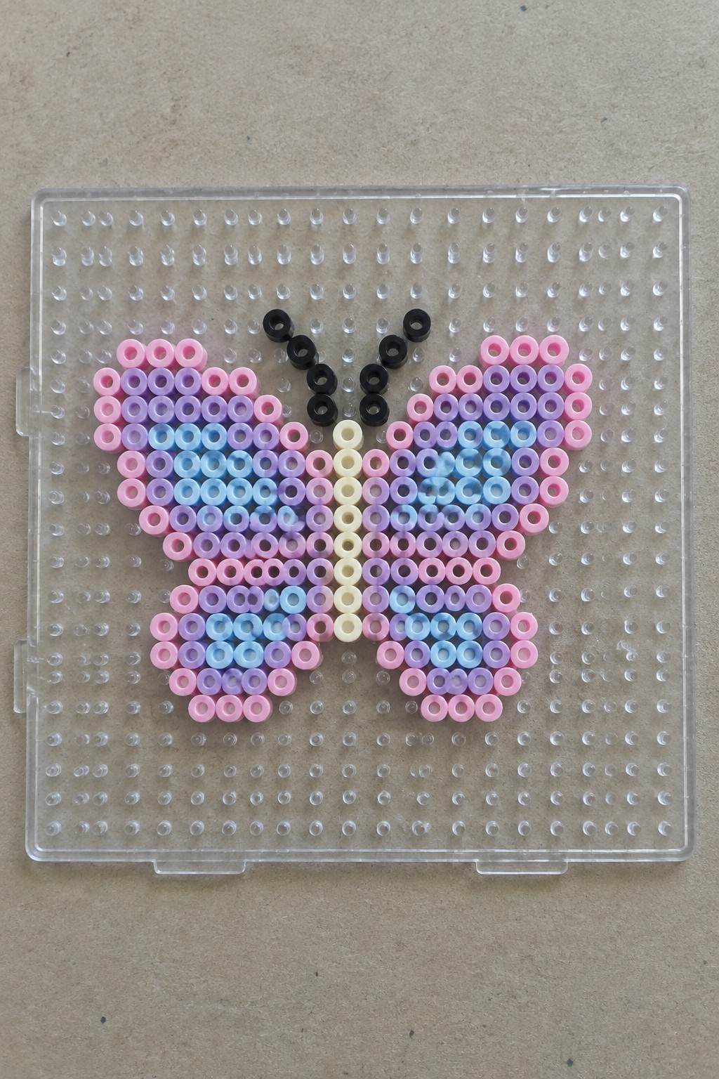 Perler bead butterfly with pink, purple, blue, and yellow wings on pegboard.