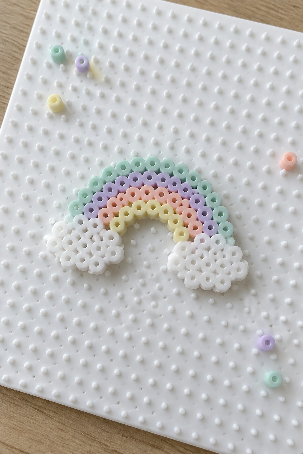 Pastel perler bead rainbow with white clouds on a pegboard