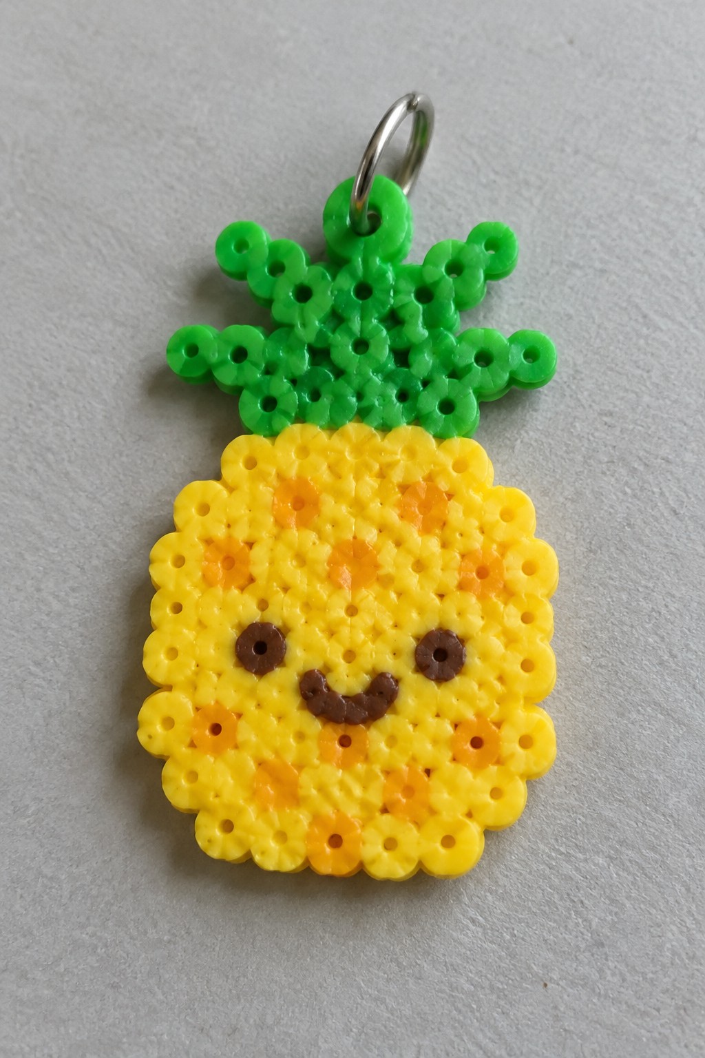 Yellow perler bead pineapple keychain with smiling face, green leaves, metal ring