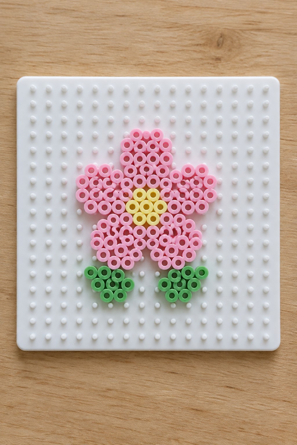 Pink perler bead flower with yellow center and green leaves on pegboard