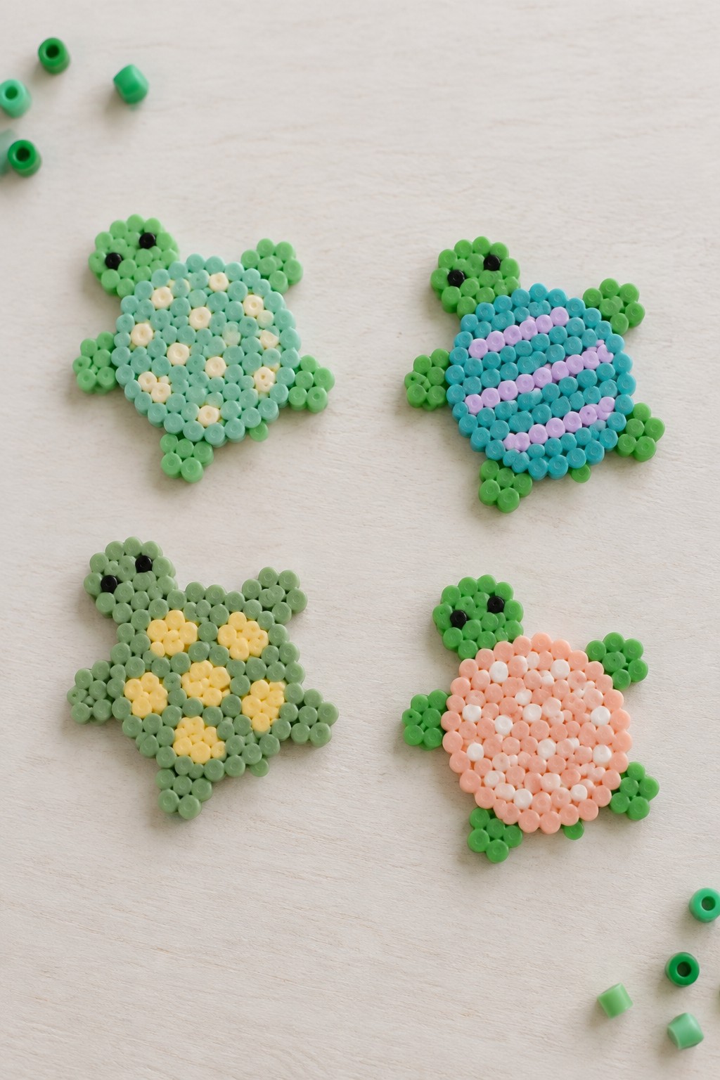 Four colorful perler bead turtles with patterned shells on white surface with loose beads.