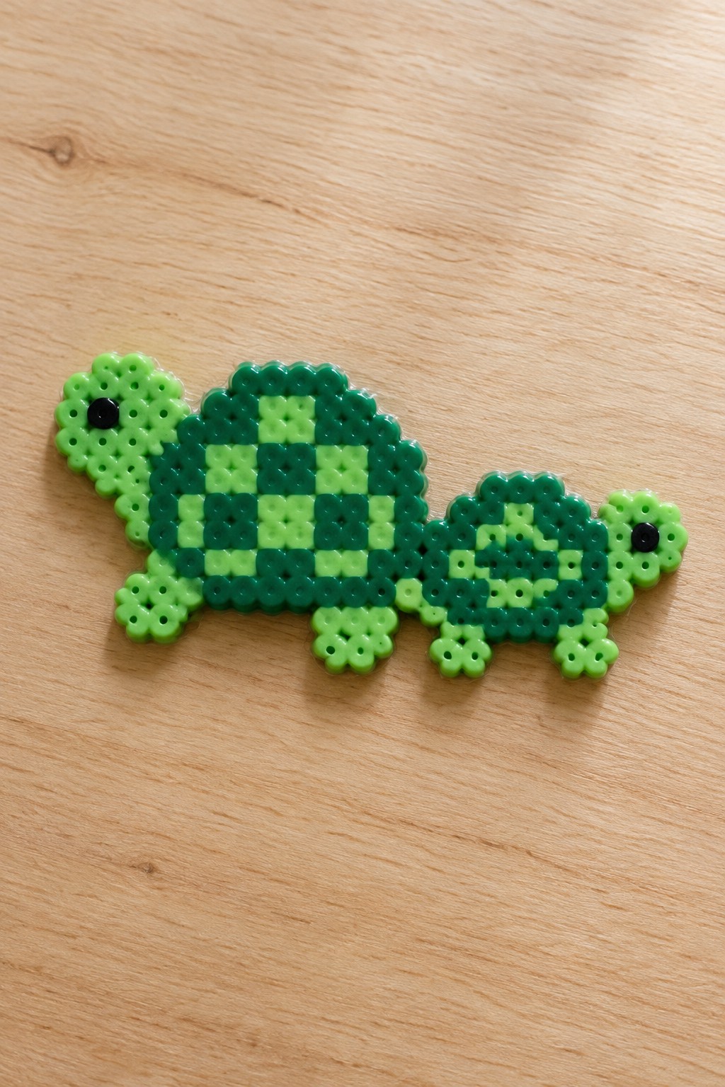 Green checkered perler bead turtle with two heads on wooden surface