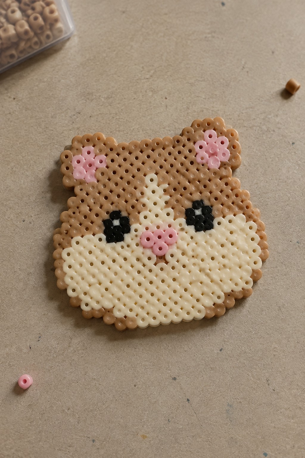 Perler bead bear face craft with brown fur, pink ears, black eyes, and white muzzle