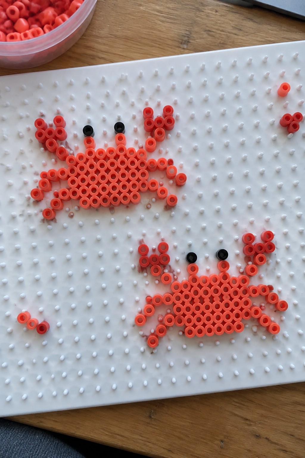 Two red perler bead crabs with black eyes on white pegboard