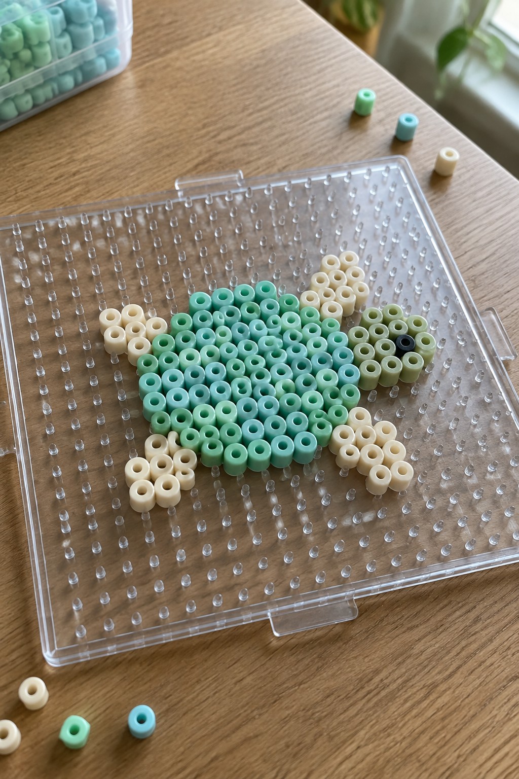 Green and beige perler beads forming a sea turtle on clear pegboard