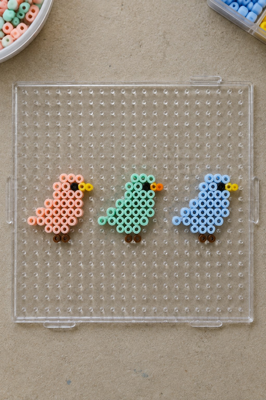 Three perler bead birds in pink, mint, and blue on clear pegboard