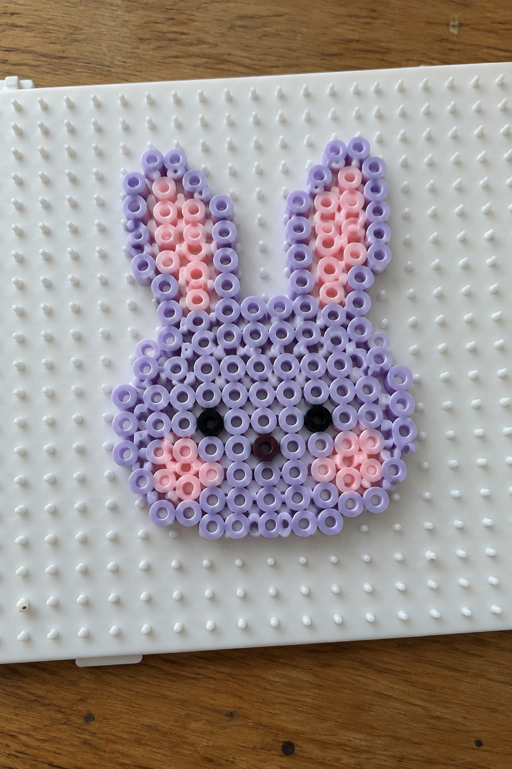 Purple perler bead bunny with pink accents, black eyes, and brown nose on pegboard