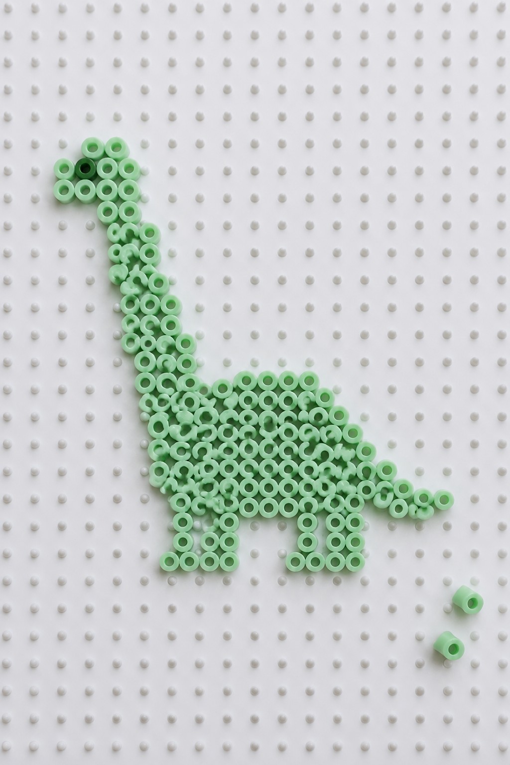 Mint green Perler beads forming a dinosaur on white pegboard with loose beads.