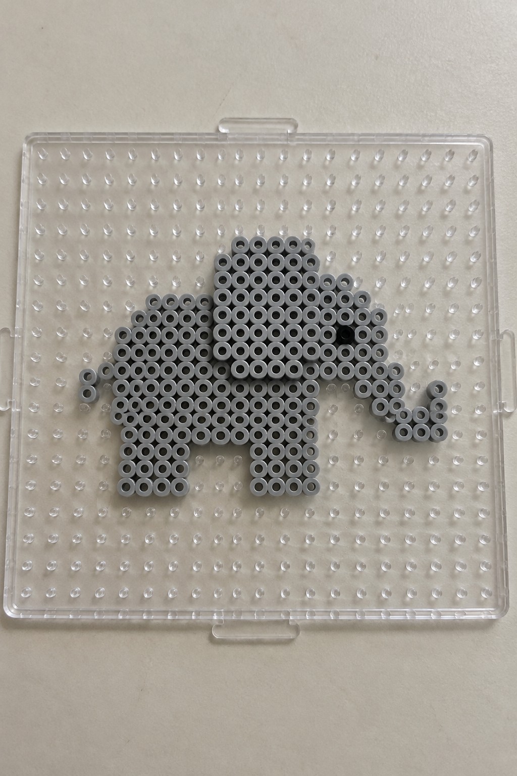 Gray perler beads form elephant shape on clear pegboard with black eye bead.