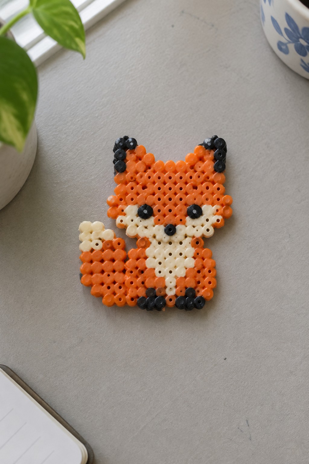 Orange perler bead fox with white face and black accents on gray surface