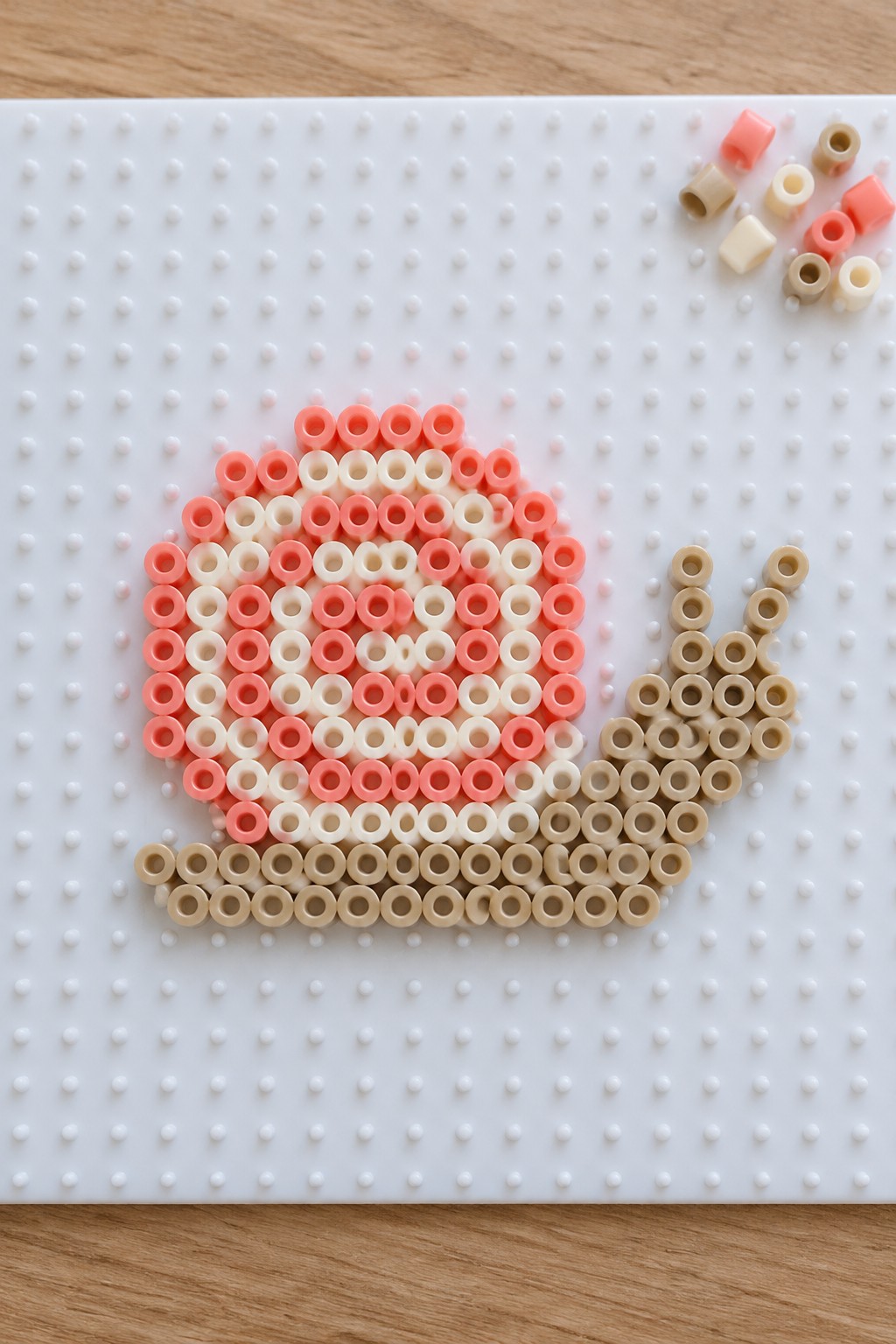 Pink and beige perler beads forming a teacup with handle on white pegboard