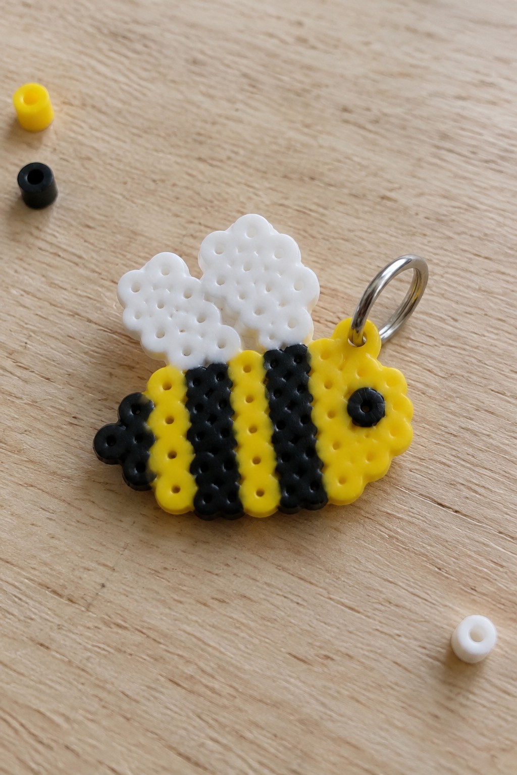 Bee keychain made of yellow black striped Perler beads with white wings on wood