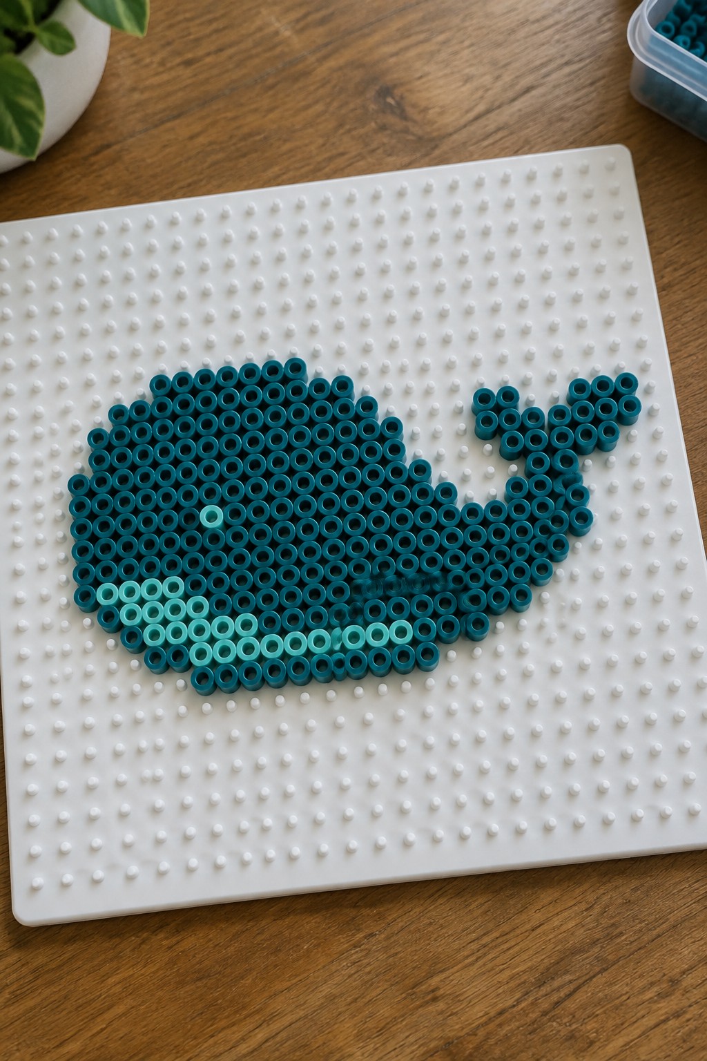 Teal perler beads forming a whale on a white pegboard