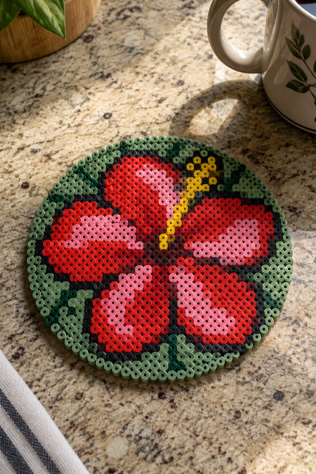 Circular perler bead ladybug coaster on speckled granite countertop beside white mug