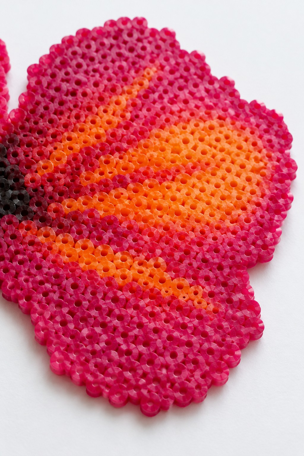 Perler bead hibiscus flower with pink-to-orange gradient on white surface