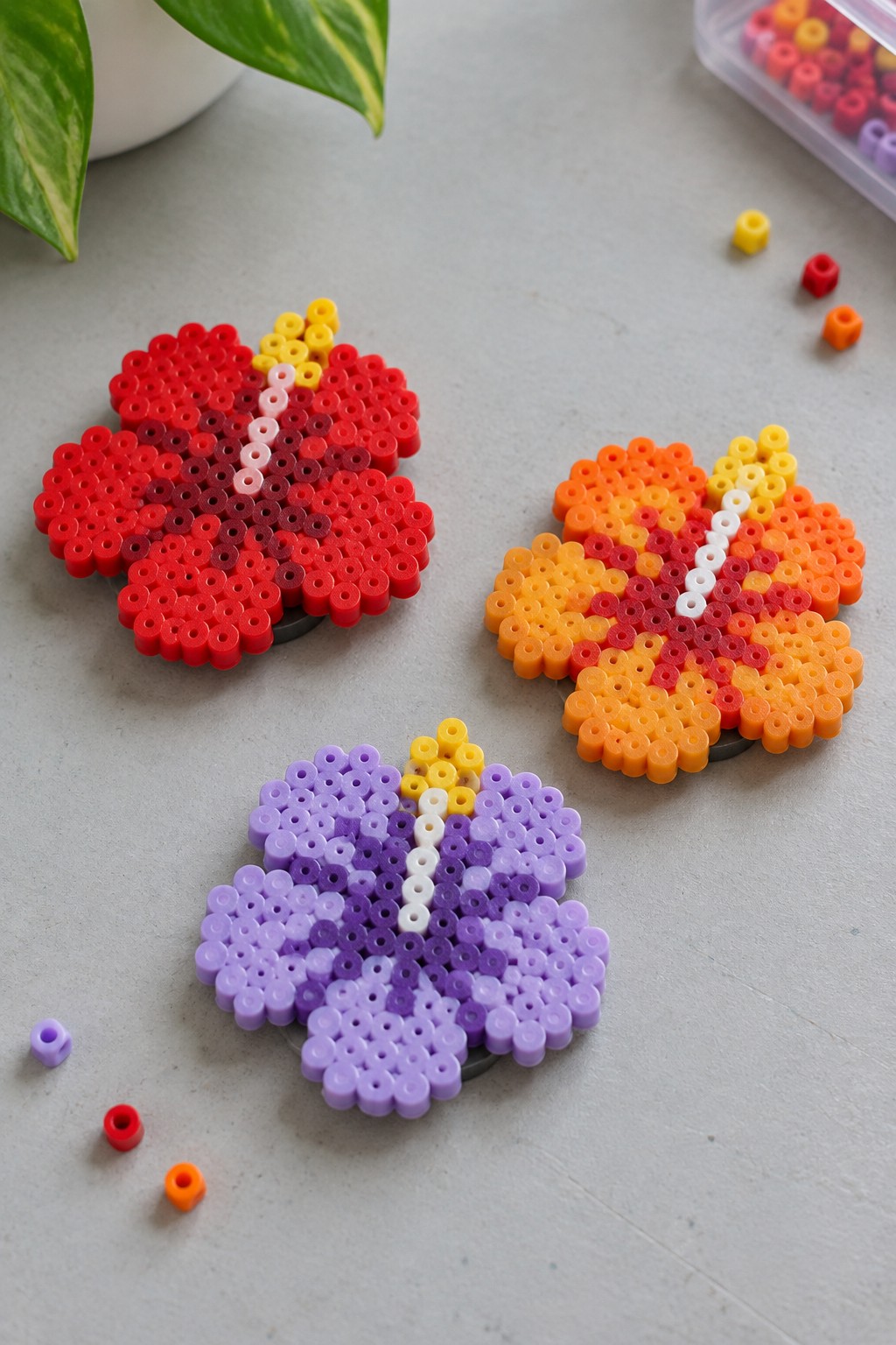 Three perler bead flowers in red, orange, and purple on gray surface