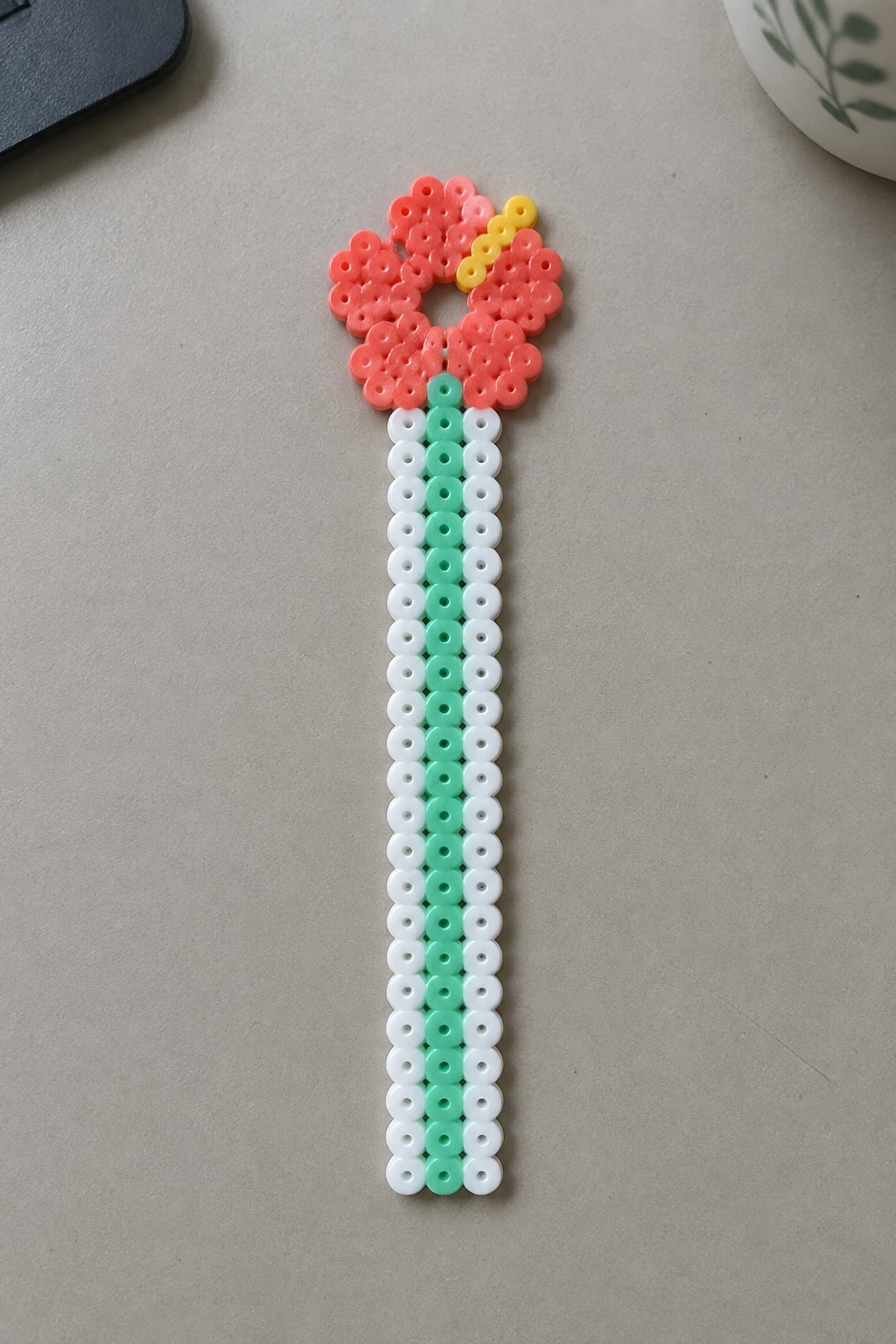 Pink perler bead flower with yellow accents and green-white striped stem