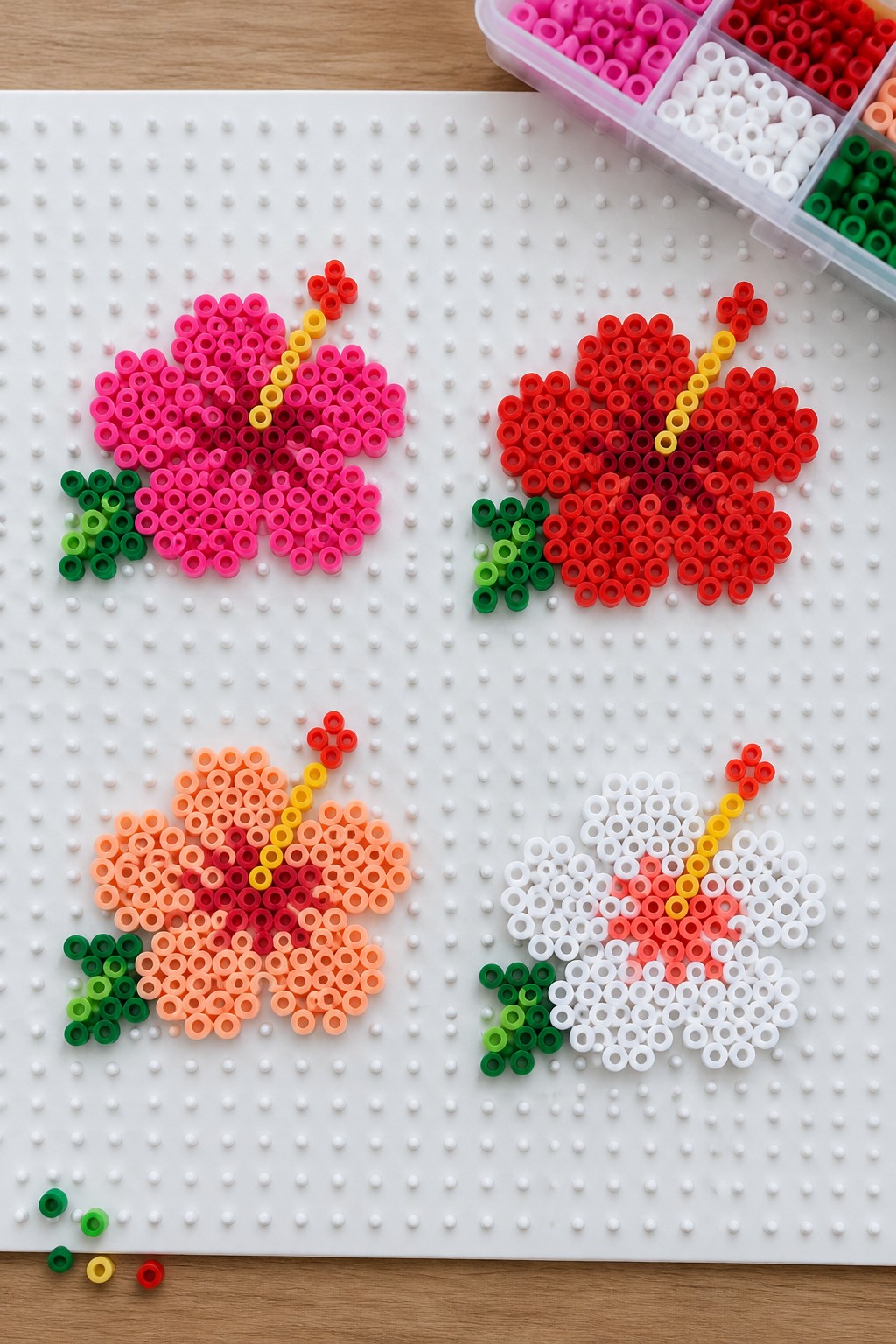 Four colorful perler bead hibiscus flowers on white pegboard with bead organizer.